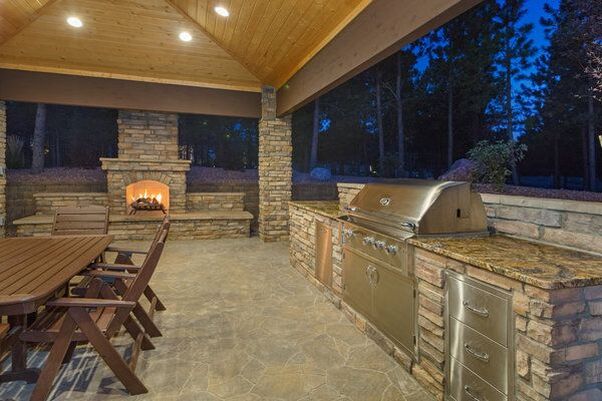Outdoor covered natural stone patio with integrated BBQ kitchen and stone fireplace